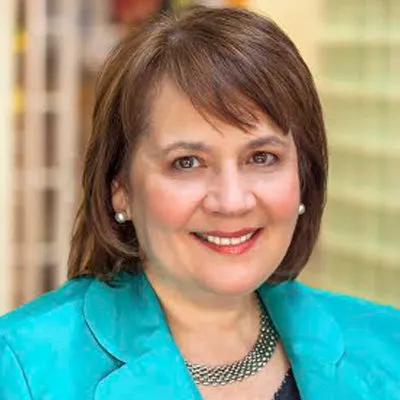 Smiling woman with short brown hair wearing turquoise blazer and silver necklace in soft focus background.