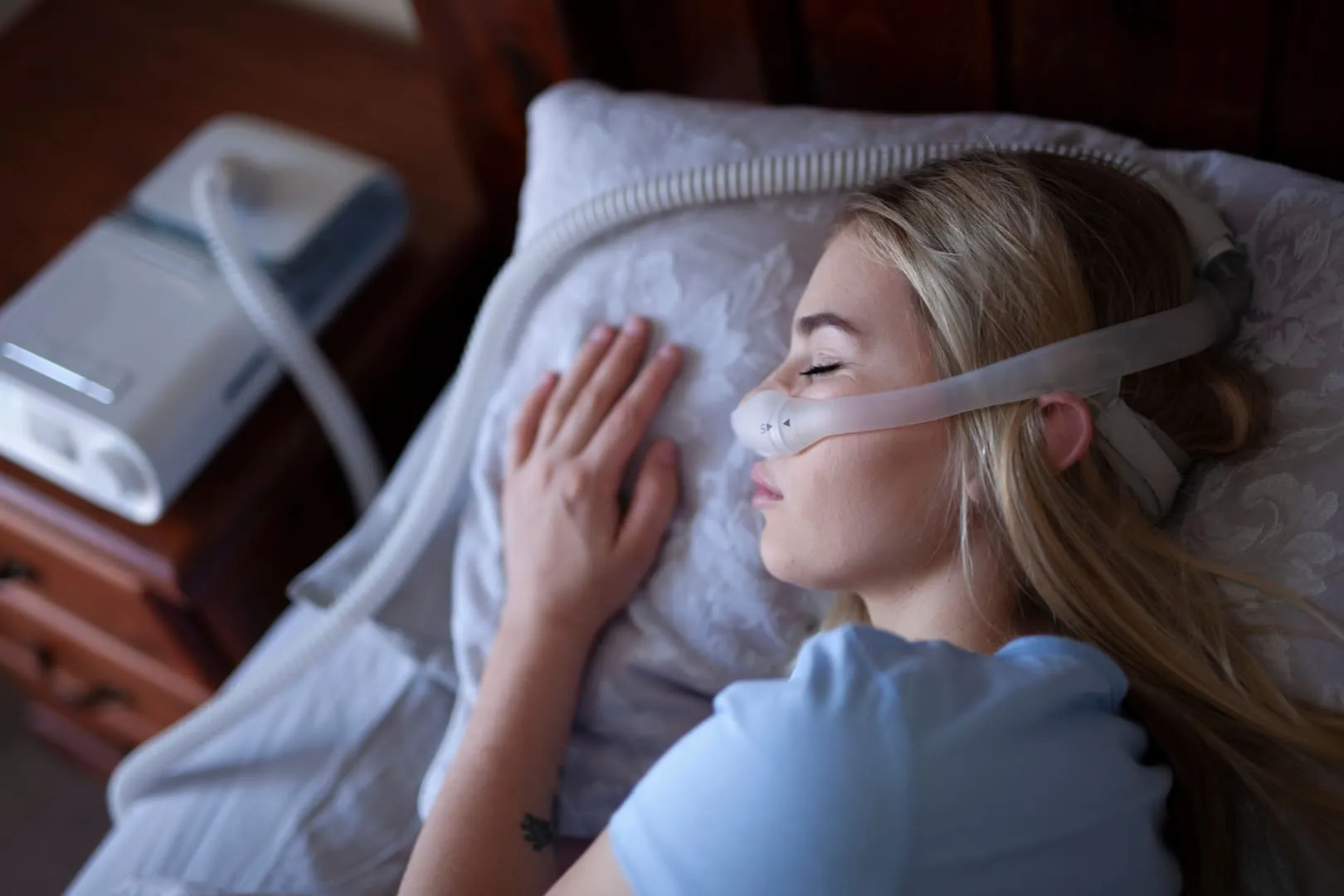 Woman sleeping on her side wearing a nasal CPAP mask connected to a machine for sleep apnea treatment.