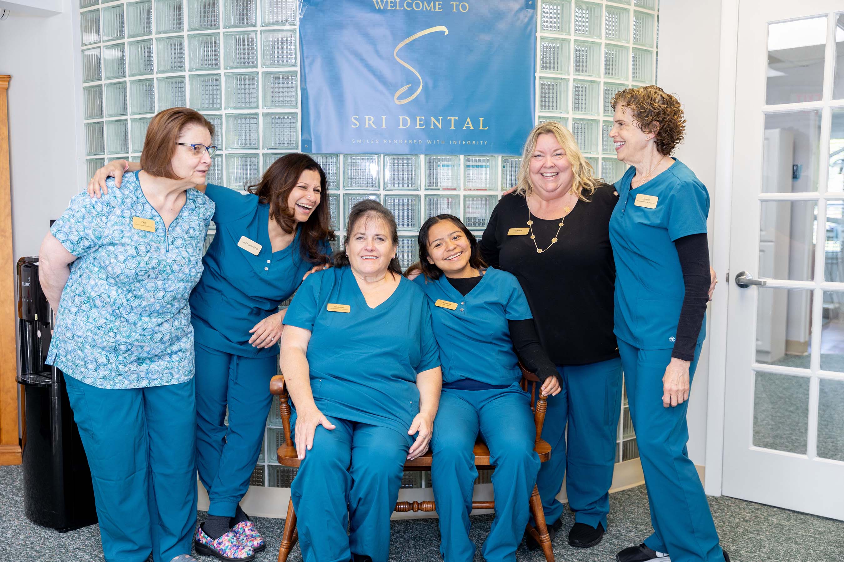 Six female dental staff smiling in front of a sign that says Welcome to SRI Dental.